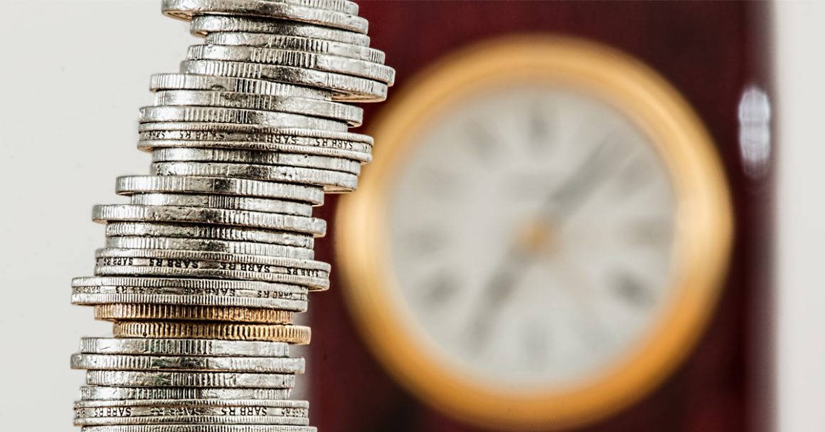 A stack of coins balanced atop a clock, symbolizing the relationship between time and money.
