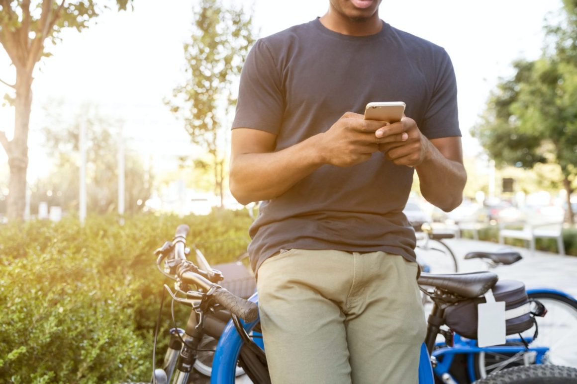 A man stands beside his bicycle, focused on his cell phone, in an outdoor setting.
